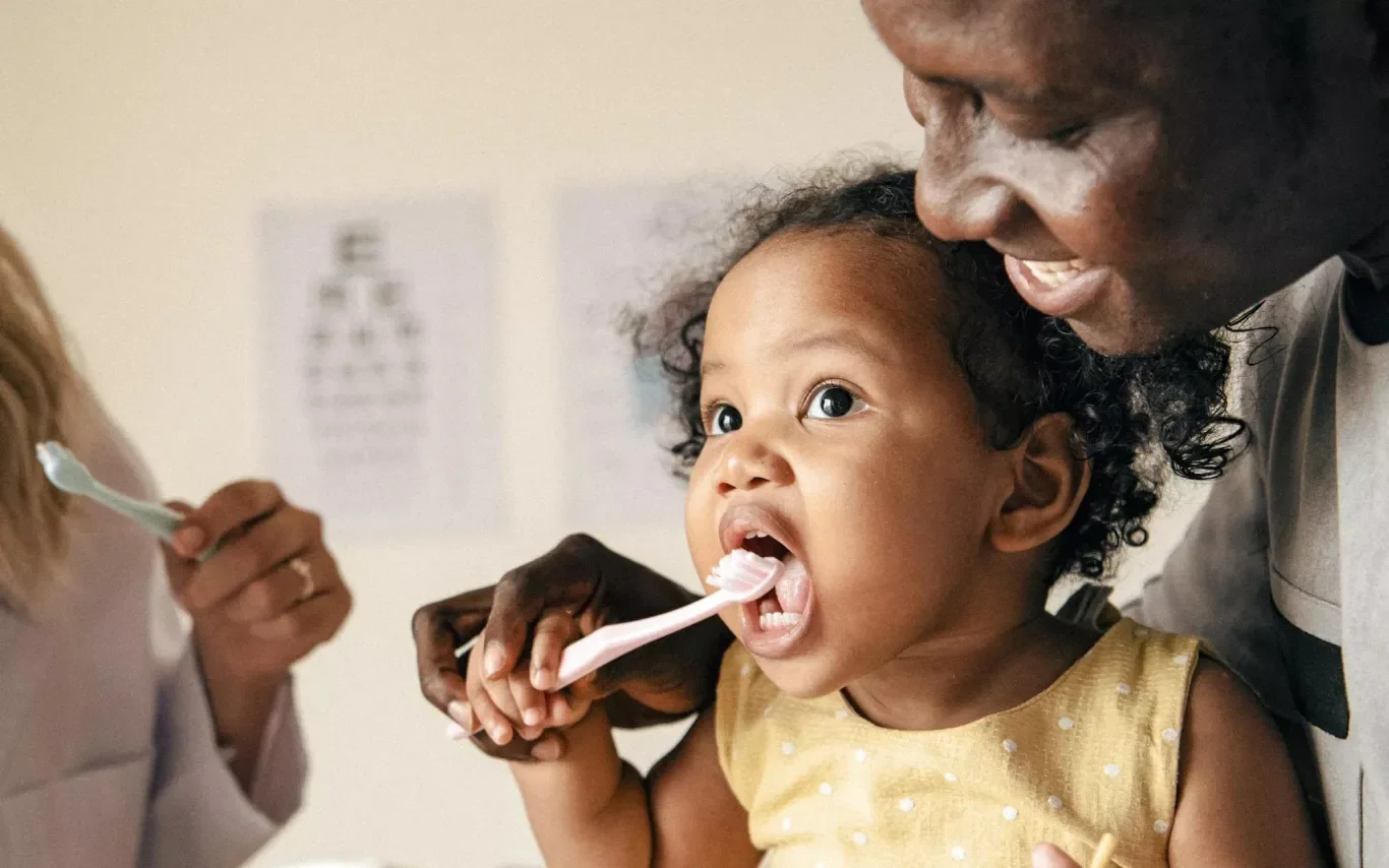 A parent helps their young child brush teeth.