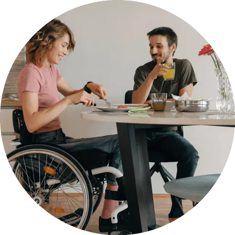 An able bodied man and a woman in a wheelchair sitting a table eating.