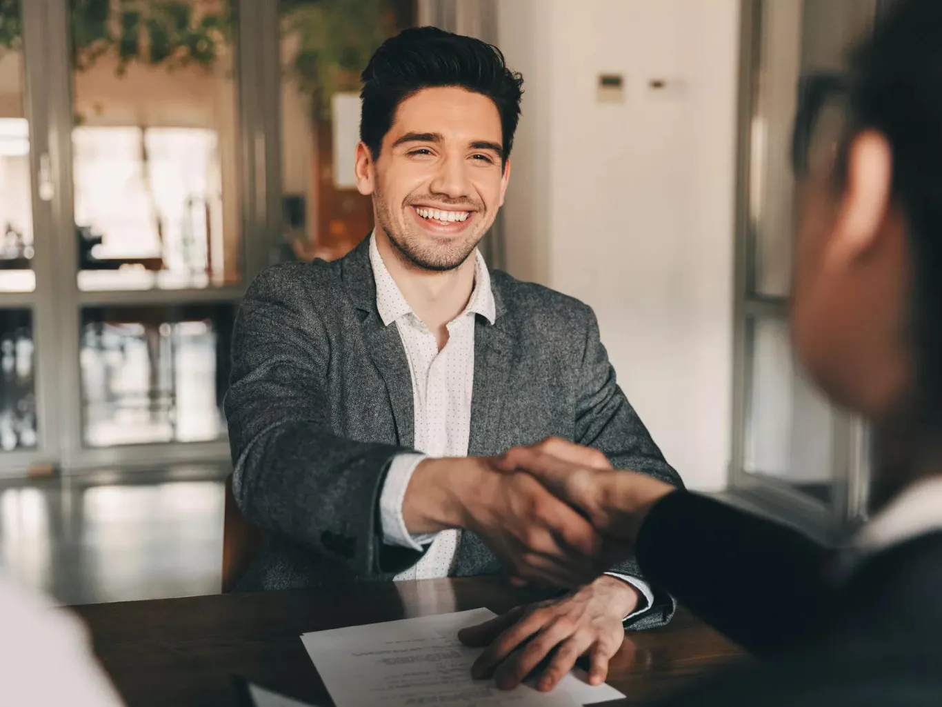 Young man shaking hands across a desk. 