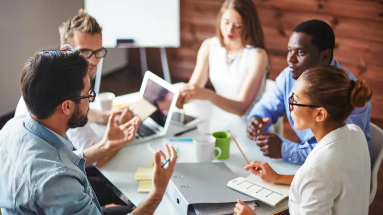 Five employees around a table discussing workplace benefits.